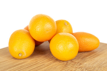 Group of six whole tasty orange kumquat on bamboo cutting board isolated on white background