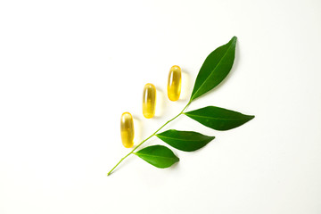 Yellow capsules with green leaves on white background.Vitamins from nature concept.