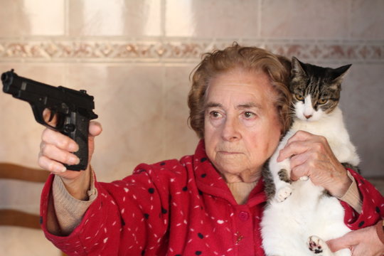Angry senior woman protecting her cat with a gun 