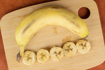 Group of one whole five slices of sweet yellow banana on bamboo cutting board flatlay on cognac leather