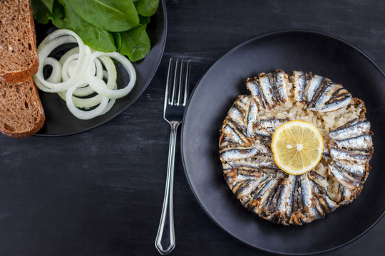 Pilaf with hamsi anchovy fish. Traditional Turkish food - Kapama Pilav - on black wooden table.