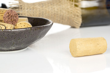 Lot of whole common wine cork  with glass bottle with jute fabric in glazed bowl isolated on white background