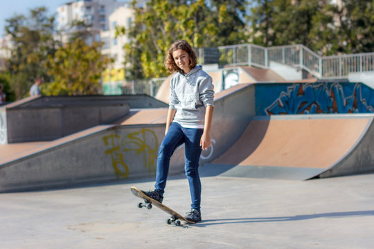 Girl teenager rides on a skateboard. Beautiful fashionable skateboarder in jeans and a hoodie on a ramp.