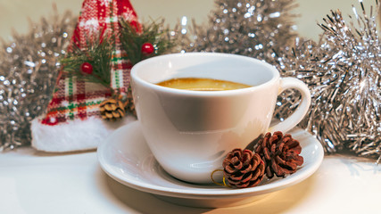 White hot cup of coffee with two cones and tinsel. Concept of christmas drink on a white background.