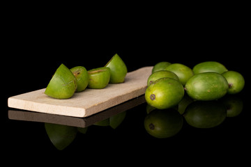 Group of lot of whole four halves of hardy green kiwi on wooden cutting board isolated on black glass