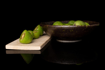 Group of lot of whole four halves of hardy green kiwi on wooden cutting board in glazed bowl isolated on black glass