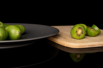 Group of four whole four halves of hardy green kiwi on gray ceramic plate on bamboo cutting board isolated on black glass