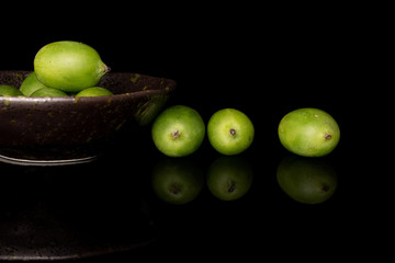 Lot of whole hardy green kiwi in glazed bowl isolated on black glass