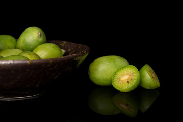 Fototapeta na wymiar Group of lot of whole two halves of hardy green kiwi in glazed bowl isolated on black glass