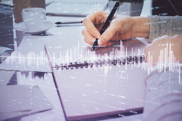 Hand taking notes in notepad. Forex chart holograms in front. Concept of research. Double exposure