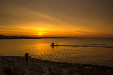 Fototapeta premium Orange sunset, boat and the people on the beach