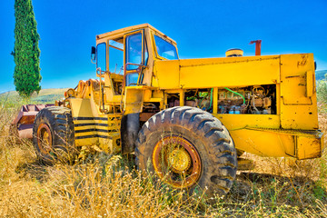 Side view of an yellow tractor in a high wheat field with rural landscape. The surrounding countryside with blue sky sunny day.