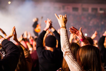 Audience with hands raised at a music festival and lights streaming down from above the stage. Soft...