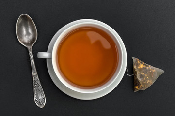 Cup of tea with tea spoon and tea bag on black.