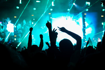 Audience with hands raised at a music festival and lights streaming down from above the stage. Soft...