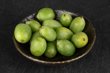 Lot of whole hardy green kiwi in glazed bowl on grey stone