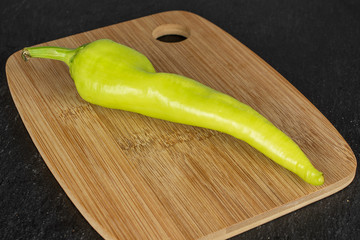 One whole hot green pepper banana on bamboo cutting board on grey stone