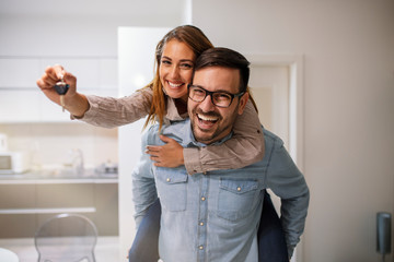 Couple showing keys to new home. Young couple holding up new house key. Portrait of young couple feeling happy about buying a new house. Happy couple moving in new home - obrazy, fototapety, plakaty