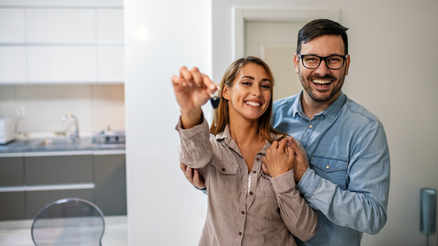 Young couple holding the keys for their new home. Couple holding a house key in their new home. They are standing in their new modern house. Both are happy and smiling.