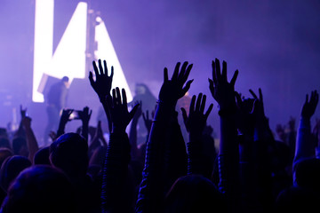 Audience with hands raised at a music festival and lights streaming down from above the stage. Soft focus, high ISO, grainy image.