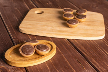 Group of eight whole sweet brown toffee on bamboo cutting board on round bamboo coaster on brown wood