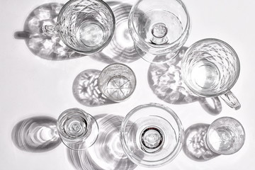 Different glasses, shot glasses and glass mugs on a white surface.  Hard light and shadow. Flatlay