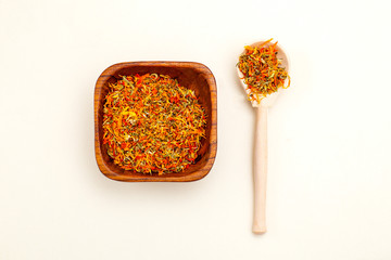 Dried calendula in a wooden bowl and wooden spoon on a light background. Apothecary herbs
