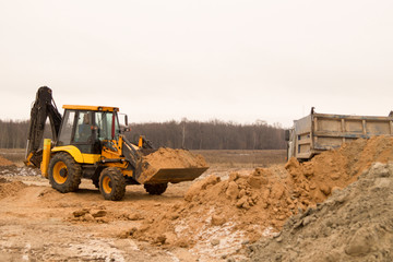 Obraz premium tractor-loader fills the earth with a bucket in the back of a truck. construction equipment.