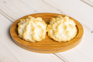 Group of two whole homemade golden coconut biscuit on bamboo coaster on white wood