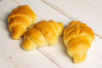 Group of three whole sweet golden mini croissant on white wood