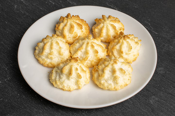 Group of seven whole homemade golden coconut biscuit on white ceramic plate on grey stone