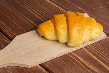 One whole sweet golden mini croissant on small wooden cutting board on brown wood