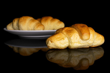 Group of three whole sweet golden mini croissant on white ceramic plate isolated on black glass