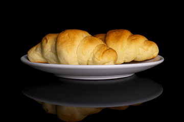 Group of two whole sweet golden mini croissant on white ceramic plate isolated on black glass