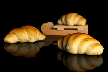Group of three whole sweet golden mini croissant with wooden sledge isolated on black glass