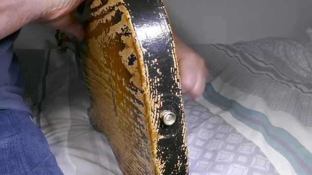 Close POV shot of man&rsquo;s hands threading a new string through a hole in the back of an old electric guitar, then pulling it through the same hole in the front, then over the neck.