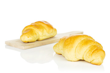 Group of two whole sweet golden mini croissant on small wooden cutting board isolated on white background