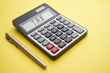 Tax Time conceptual with calculator and gold pen on yellow background