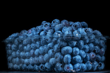 Fresh blueberries in disposable plastic food pack on black background. Close-up of Bog bilberry,...