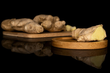 Group of two whole one piece of fresh brown ginger on bamboo cutting board on round bamboo coaster isolated on black glass