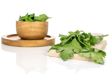 Lot of whole lot of pieces of fresh green parsley on round bamboo coaster in bamboo bowl on wooden cutting board isolated on white background