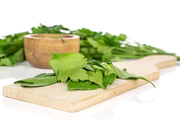Lot of whole lot of pieces of fresh green parsley in bamboo bowl on wooden cutting board isolated on white background