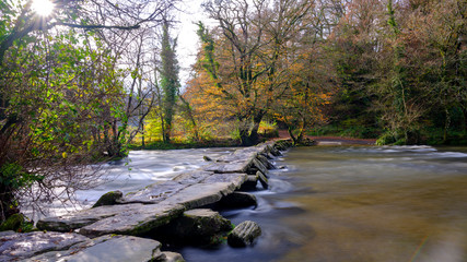 Obraz premium Tarr Steps with a full flowing river Barle and autumn colours, Exmoor