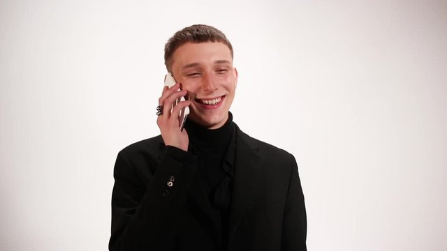 Man in a black suit with earrings talking on the phone and smiling, white background
