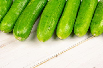 Group of seven whole fresh green baby cucumber on white wood