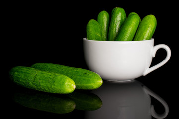 Group of seven whole fresh green baby cucumber in white ceramic cup isolated on black glass