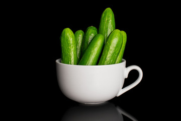 Group of seven whole fresh green baby cucumber in white ceramic cup isolated on black glass