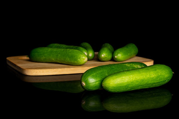 Group of seven whole fresh green baby cucumber on bamboo cutting board isolated on black glass