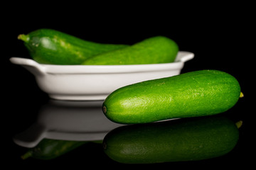 Group of three whole fresh green baby cucumber in white oval ceramic bowl isolated on black glass