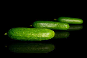 Group of three whole fresh green baby cucumber placed diagonally isolated on black glass